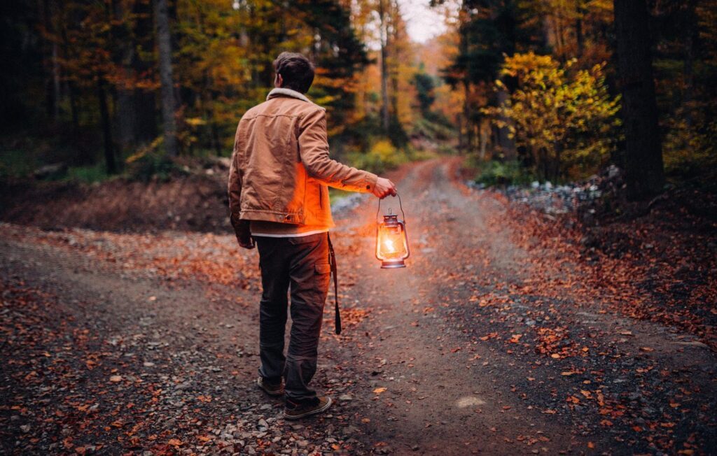 A man with a lamp on a road in the middle of the forest.