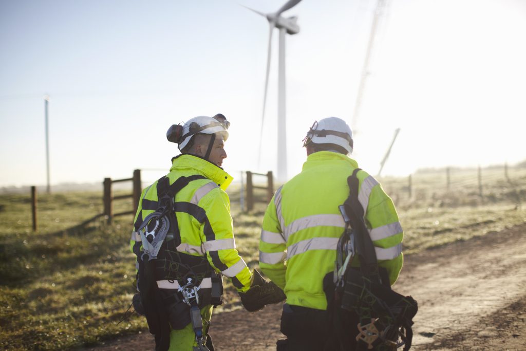 Two engineers at wind farm, walking together, rear view