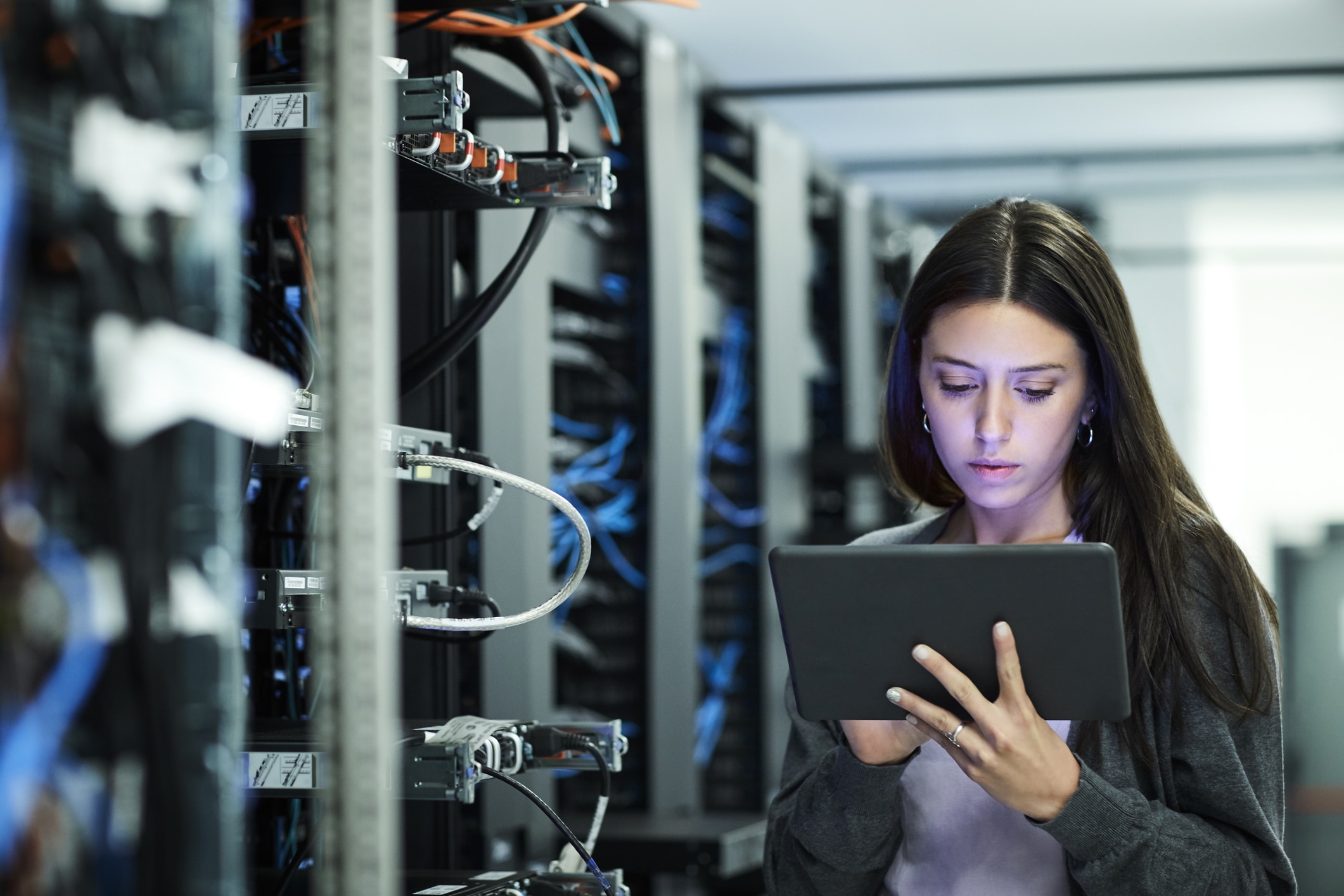 Female technician using digital tablet in server room. IT professional is standing at workplace.