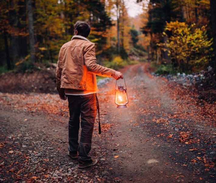 A man with a lamp on a road in the middle of the forest.