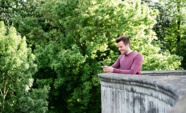 Man using smart phone whilst leaning over low wall