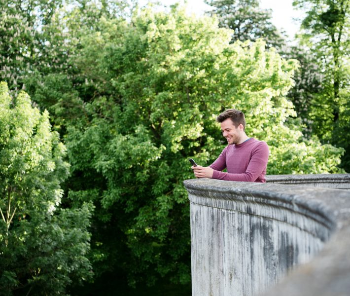 Man using smart phone whilst leaning over low wall