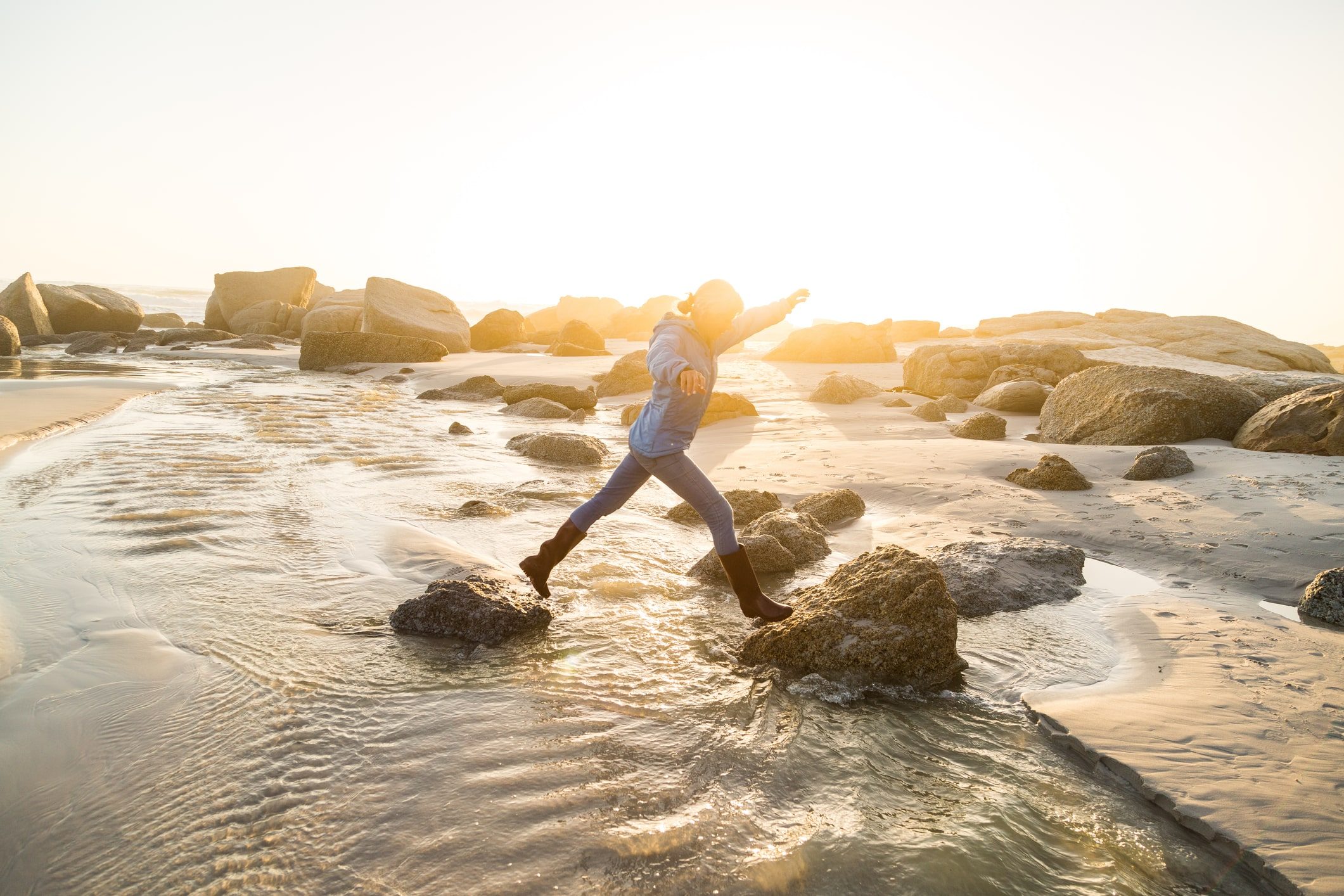 Woman stepping across stream on the beach at sunset