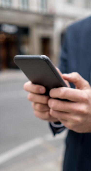 Close-up on a business man texting on the phone in the street and carrying the newspaper