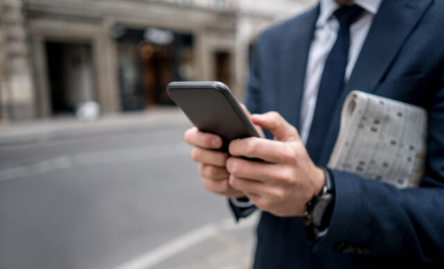 Close-up on a business man texting on the phone in the street and carrying the newspaper