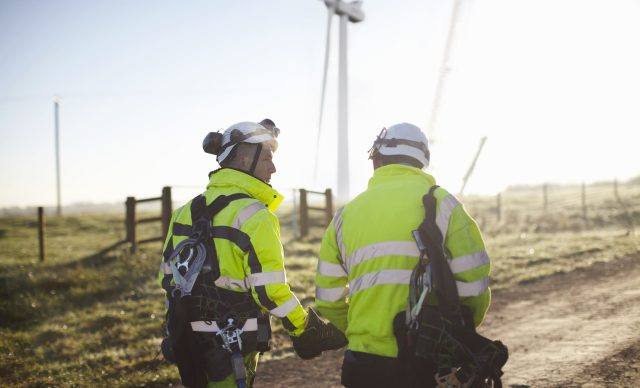 Two engineers at wind farm, walking together, rear view