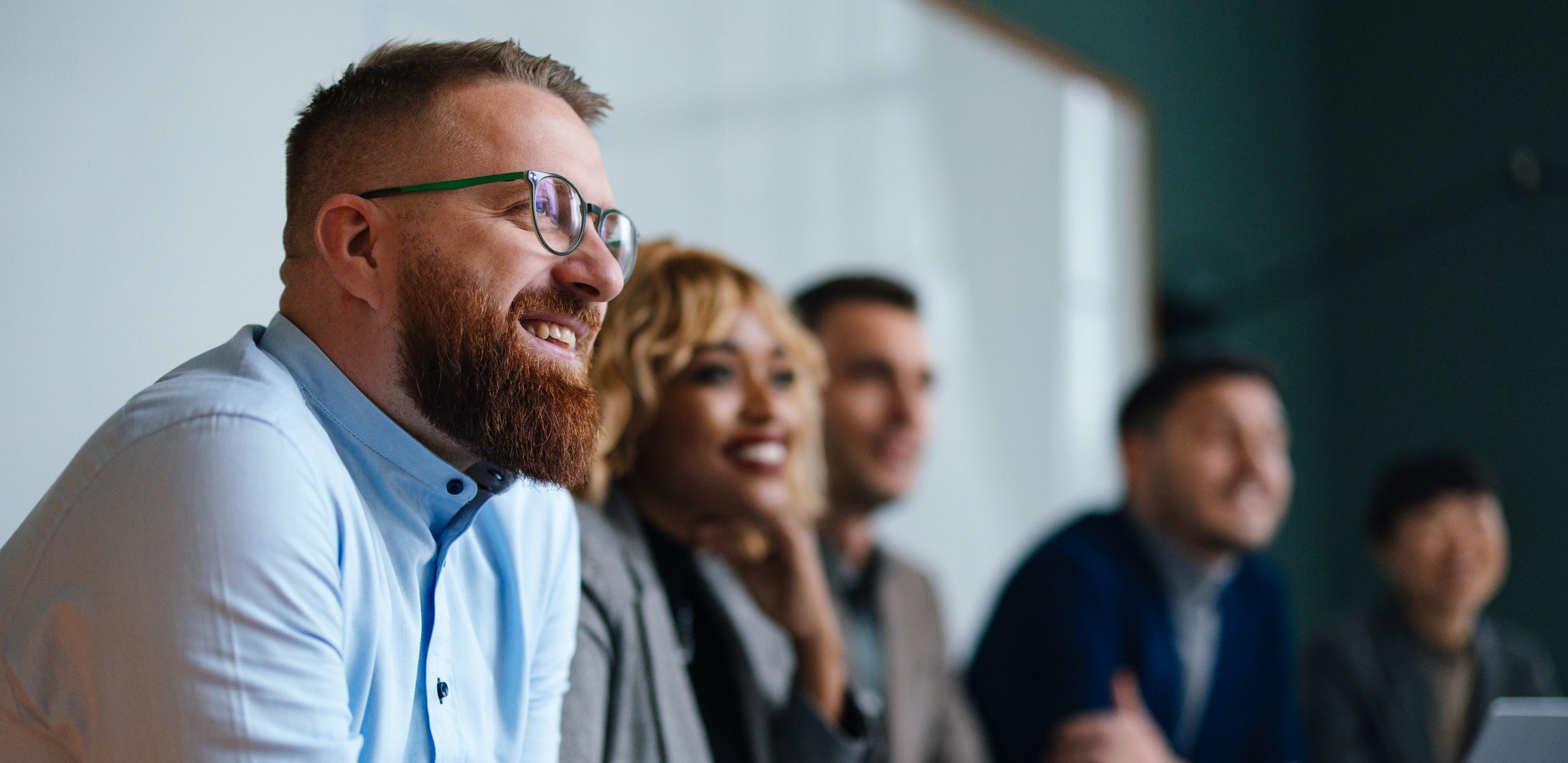 Smiling businessman and unrecognizable multi-ethnic employees sitting in a row at their company desk and listening to their boss.