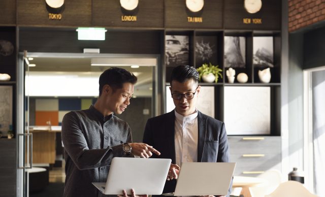 Two handsome Chinese men standing with laptops in an office