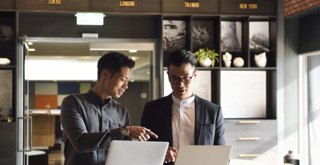 Two handsome Chinese men standing with laptops in an office