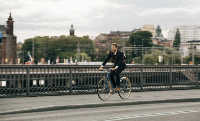 Businessman riding bicycle on street in city against sky