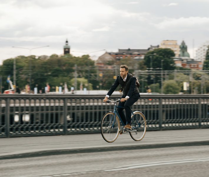 Businessman riding bicycle on street in city against sky