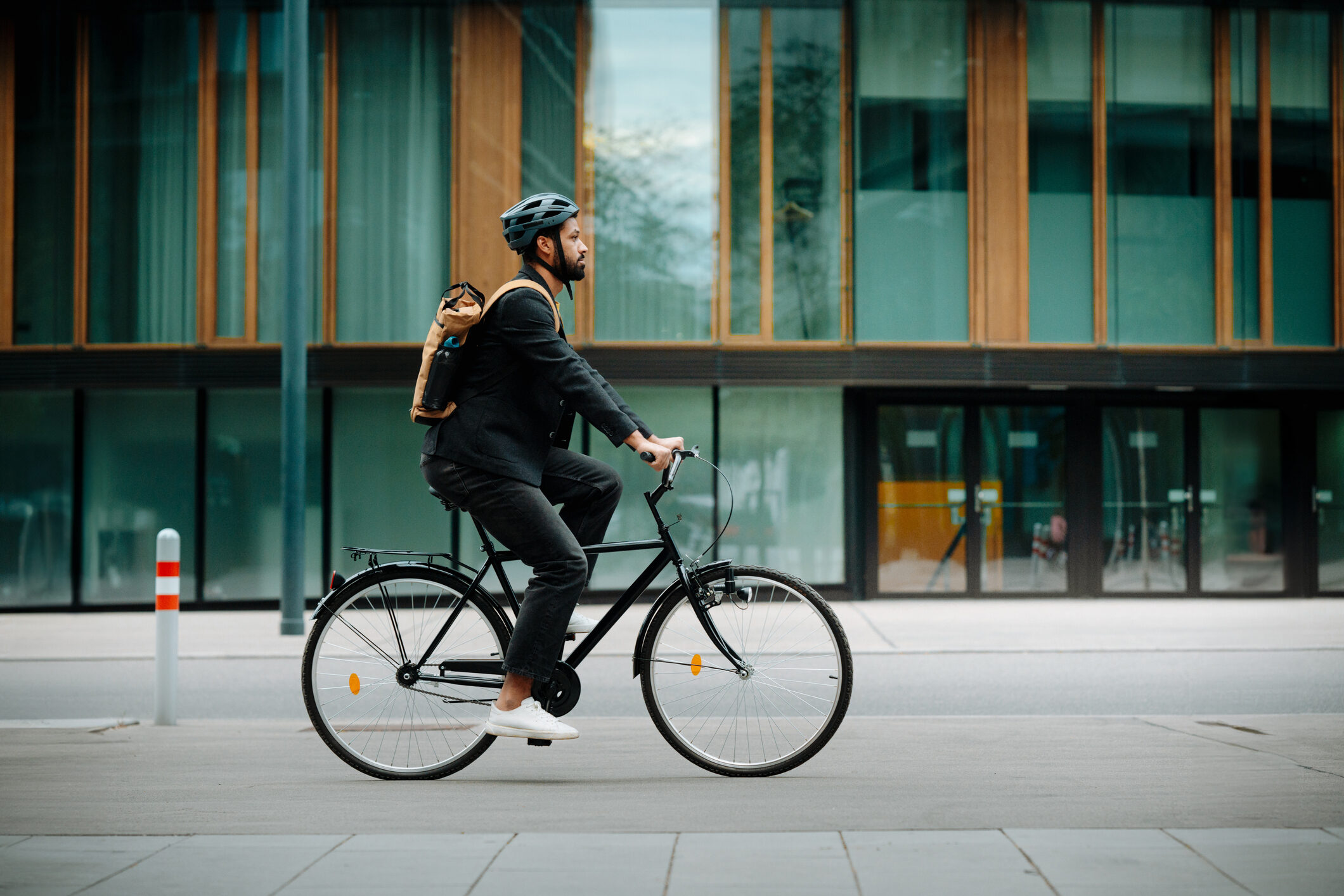 Side view of a city commuter riding to work on a bicycle. Young single businessman traveling from work to home on a bike, wearing a backpack and helmet for safety. City lifestyle of single man.