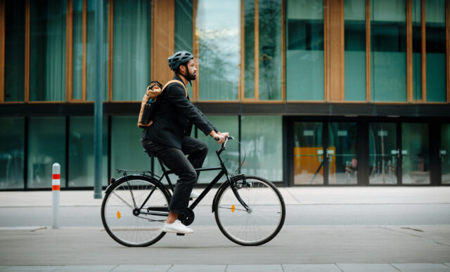 Side view of a city commuter riding to work on a bicycle. Young single businessman traveling from work to home on a bike, wearing a backpack and helmet for safety. City lifestyle of single man.