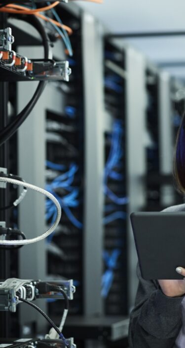 Female technician using digital tablet in server room. IT professional is standing at workplace.
