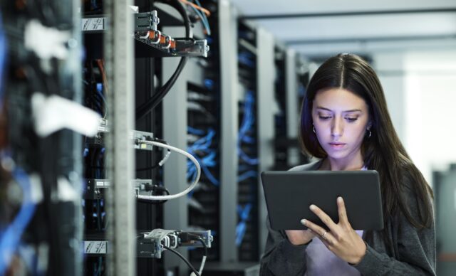 Female technician using digital tablet in server room. IT professional is standing at workplace.