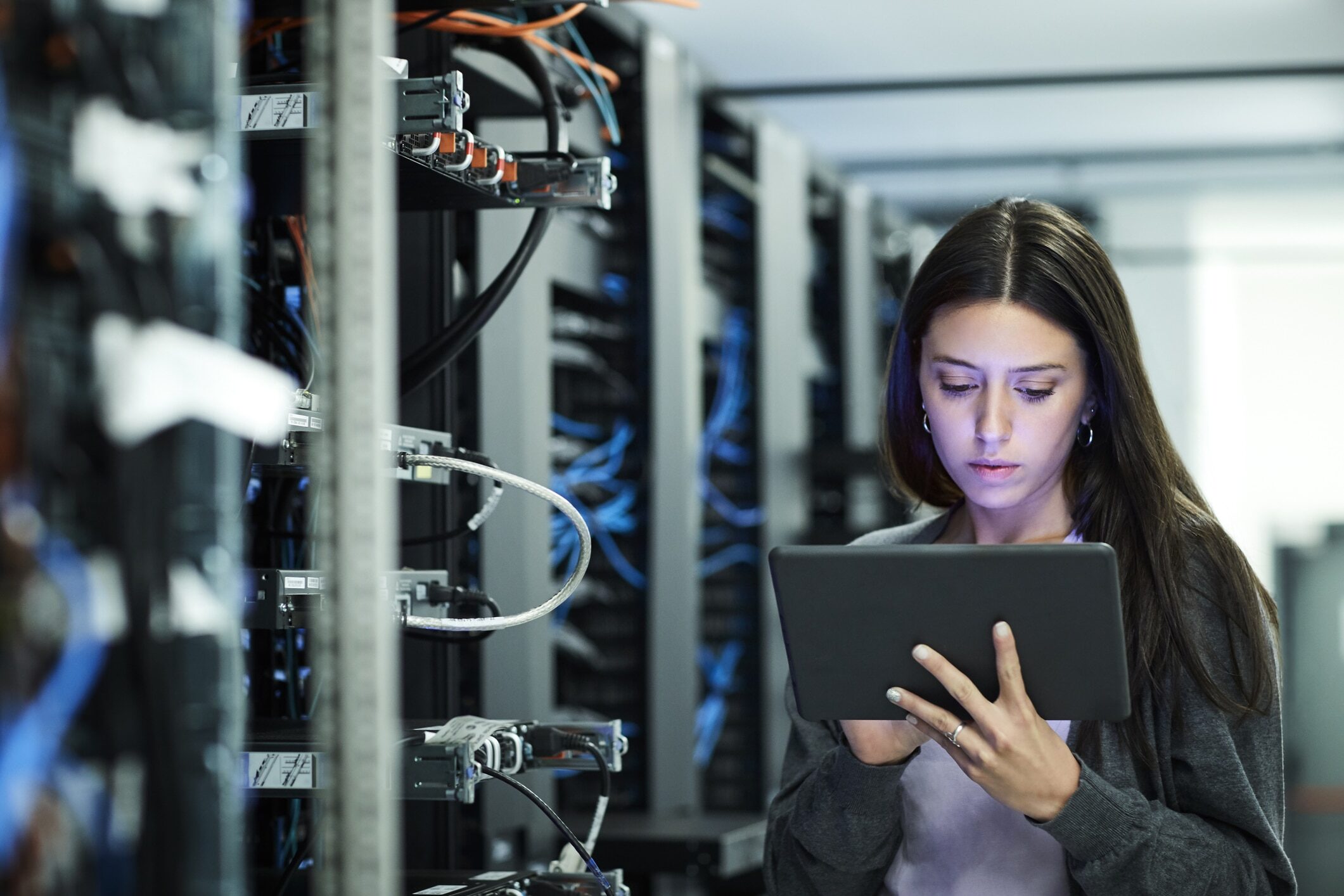 Female technician using digital tablet in server room. IT professional is standing at workplace.
