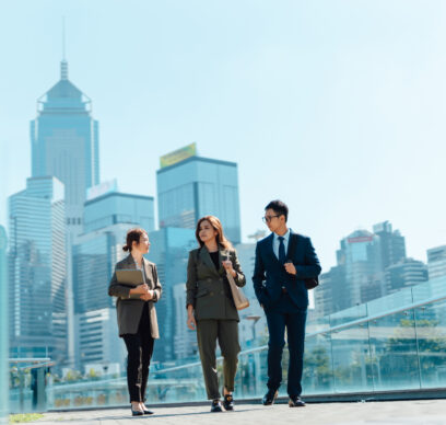 Three confident and successful Asian business people having a discussion on the go, walking in financial district against urban skyline. Teamwork and collaboration. Striving for success. Overcoming challenges and reaching goals.