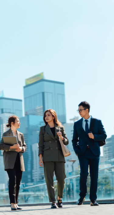 Three confident and successful Asian business people having a discussion on the go, walking in financial district against urban skyline. Teamwork and collaboration. Striving for success. Overcoming challenges and reaching goals.