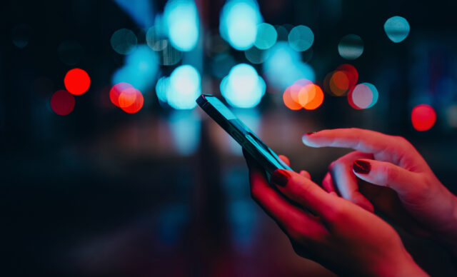 Young woman networking with social media on smartphone in city street at night