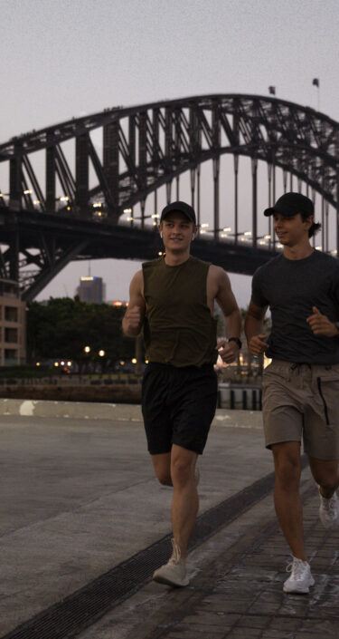 A shot of two young, Caucasian males running along Sydney Harbour, Australia.